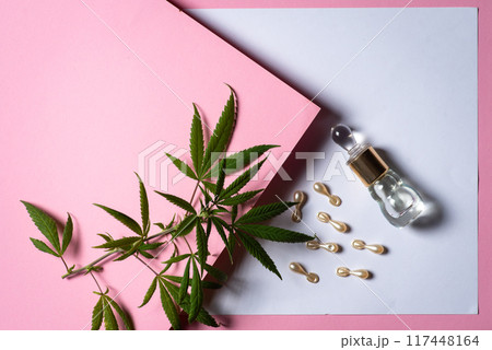 Marijuana leaves, hair capsules and perfume bottle on light pink and purple paper background 117448164