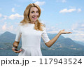 Blonde woman with tablet device and shows copy space. Mountain landscape in the background. 117943524