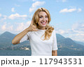 Portrait of charming mature woman standing outdoors showing call me back gesture sign. Mountain landscape in the background. 117943531