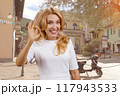 Portrait of a happy cheerful mature caucasian blond woman shows ok gesture sign outdoors. City street in the background. 117943533