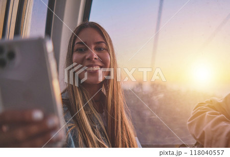 Young tourist sitting on the cableway in Caracas enjoying a photo taken on her smartphone. Bright sky, clouds and mountains. Selective focus 118040557