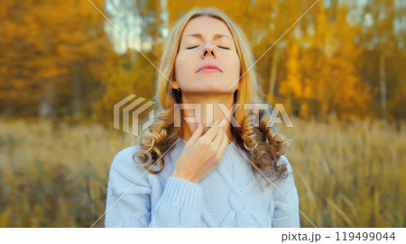 Sick exhausted woman suffering from acute sore in throat flu, touches neck with hand outdoor in park 119499044