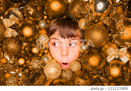 Surprised little boy face with joy in golden Christmas tree toys balls. Holiday. 111211909