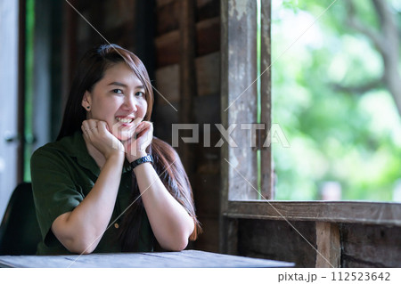 Happy of Portrait Happy Smiling beautiful Asian woman wearing brownish green dress stylish hipster with beside the window of a wooden house background 112523642