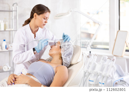 Aesthetician administering facial procedure on young woman using ultrasonic shovel 112602801