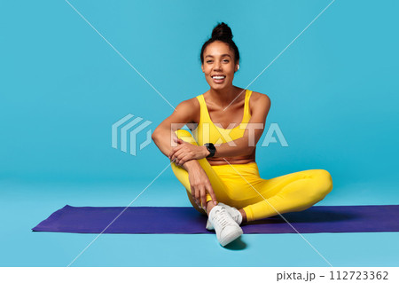 black lady in activewear with tracker sits on mat, studio 112723362