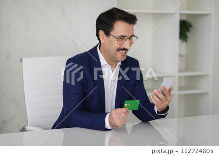 Smiling businessman in a blue suit happily checking his smartphone 112724805