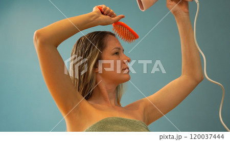 A woman is expertly styling her hair using a blow dryer and brush while in the bathroom 120037444