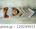 A cheerful boy lies on the floor, and above his head there is a large stack of books in the form of a roof. 120249915