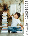 A boy sits next to a stack of books and holds them with his hand 120249925