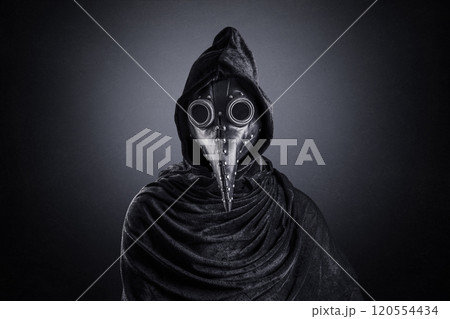 Plague doctor in hooded cloak at night over dark misty background 120554434