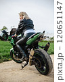 A stylish woman in leather pants and a black jacket sits confidently on a green motorcycle. The 120651147