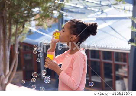 Blowing bubbles, african american girl enjoying outdoor activity at school playground with friends 120616579