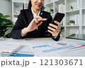 business woman using smartphone while working on laptop, synchronize data between computer and gadget at home, use corporate devices and business application 121303671