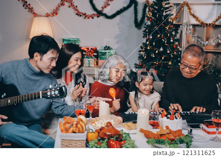 Multi-Generation Family Celebrate Christmas At Home Wearing Santa Hats And Antlers Opening Presents 121311625