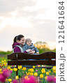 Happy mother and toddler son hugging sitting on a bench along a field of tulips. Family spending time, lifestyle concept 121641684