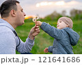 Father and toddler son holding dandelion and blowing on it. Family spending time and lifestyle concept. Focus on man's hand 121641686