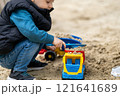 Little cute toddler boy three years old plays in the sandbox on a spring day. Outdoor development activities for kids. Toy cars and shovel. Focus on the car 121641689