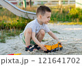 Little cute caucasian toddler boy of three and a half years old plays in the sandbox on a sunny summer day. Outdoor creative activities for kids. Toy dump truck and shovel. 121641702