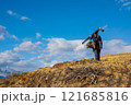 Photographer walks through dry landscape carrying camera gear and equipment 121685816