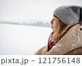 Girl bundled in thick blanket standing on balcony and looking at snowfall. 121756148