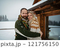 Couple hugging in front of a cabin during snowfall. Romantic weekend trip for mature couple. 121756150