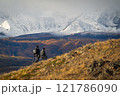 Hikers exploring a scenic mountainous landscape with golden foliage and snowy peaks 121786090