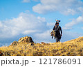 Photographer hiking with camera gear through grassy landscape under blue sky 121786091