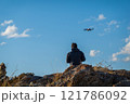 Man with a drone flying above rocky outdoor surroundings under a blue sky 121786092