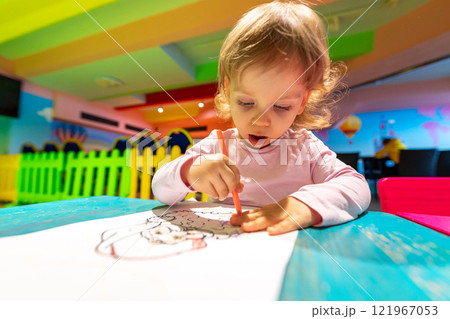 A creative child coloring at a colorful table in a vibrant indoor play area. 121967053