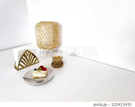 Cozy minimalist dessert setup with cake, coffee, and lamp on white table 122415435