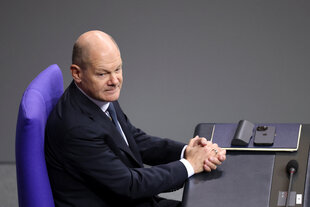 Olaf Scholz sitzt auf dem Regierungssessel im Bundestag und hat die Hände gefaltet