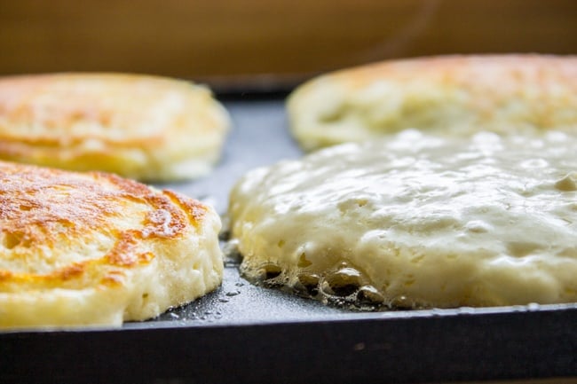 Pancakes on griddle puffing up and bubbling around the edges.