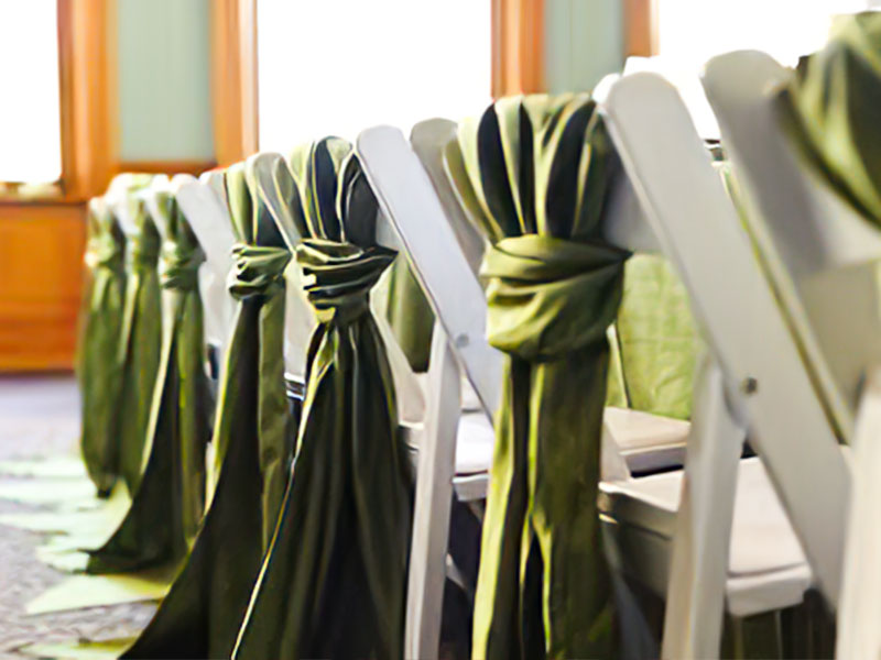 White floding chairs in a row with green linen drapes hanging off the back of the chairs.