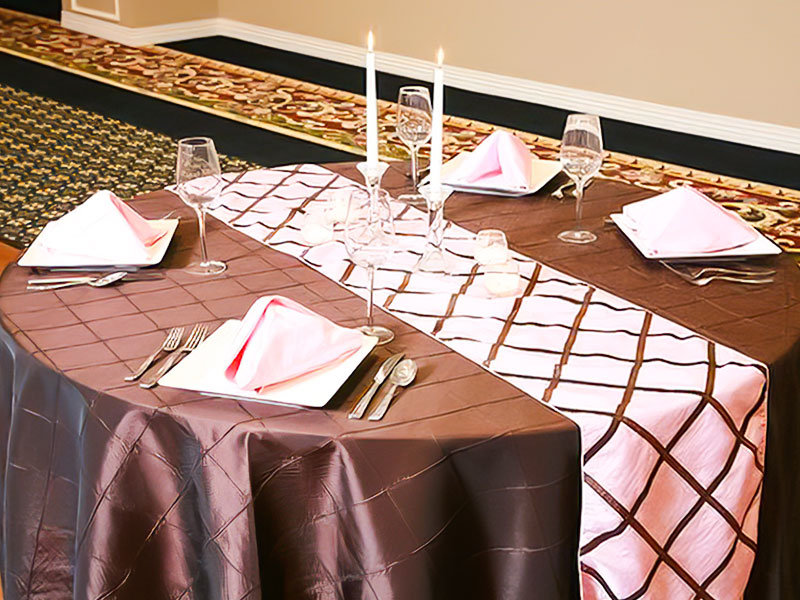 Brown table linen with a white and brown runner in the middle of the table with place settings and candles on the table.