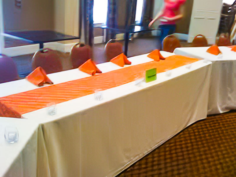 Tables with white skirtless banquet linens with orange accent cloths inside for an event.