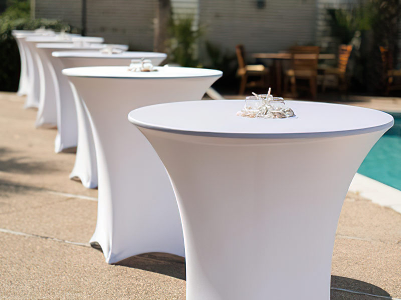 Highboy tables lined up outside with spandex covers on them.