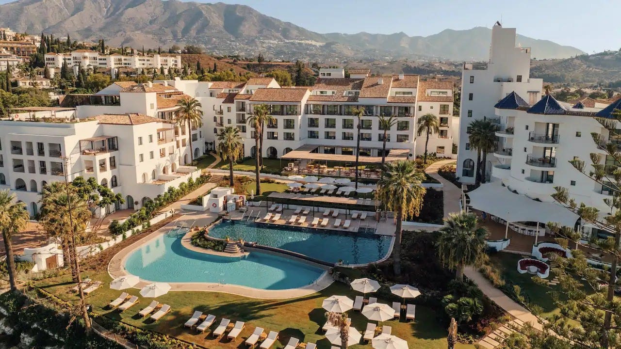 Four- and five-story white buildings surrounding a pool with lounge chairs and umbrellas.