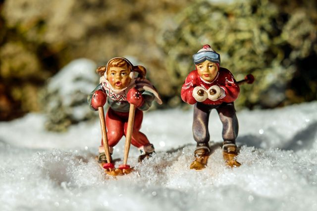 This festive winter scene features miniature skiers in vibrant attire, set in a snowy environment. Ideal for use in Christmas and winter holiday promotions, gift store displays, or craft and hobby magazines. Highlights themes of winter activities, festive decor, and holiday cheer.