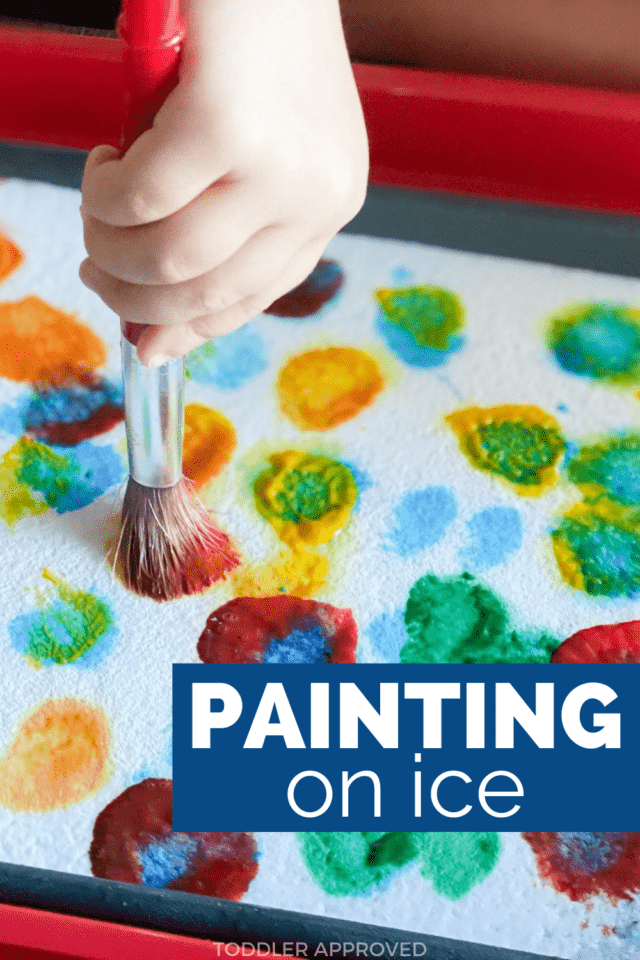 little girl's hand holding paintbrush and painting on ice with paint