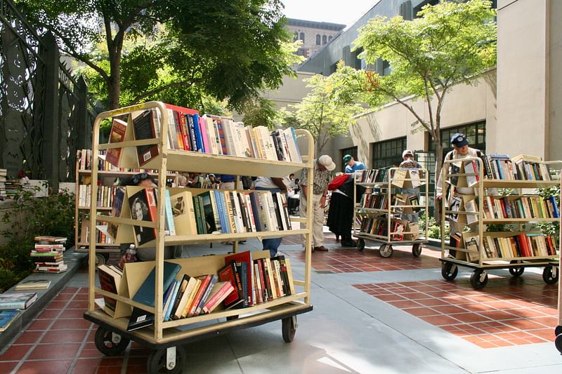 Carts of books in a courtyard at the Los Angeles Central Library with people browsing.