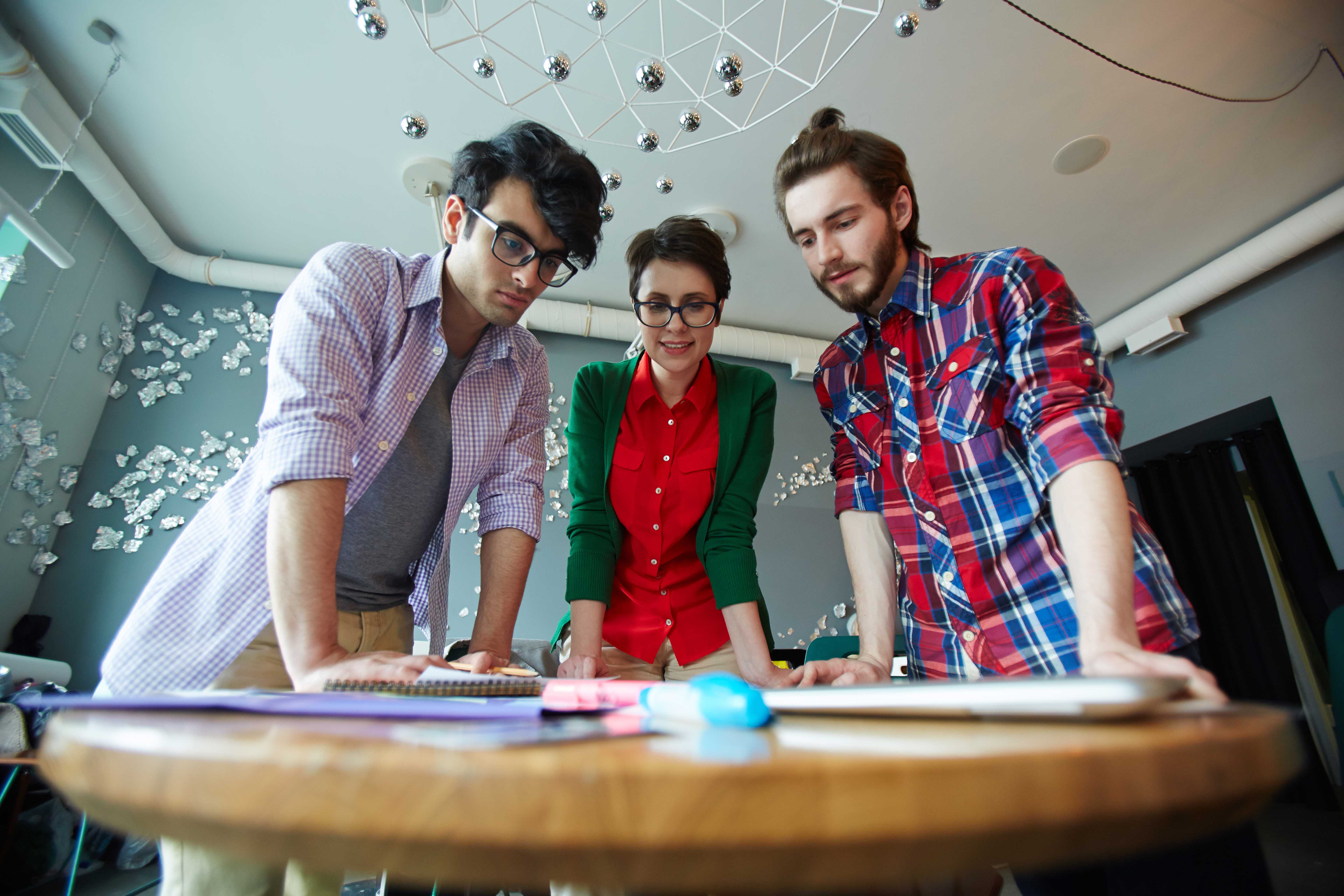 Low angle image of three people standing around a table.