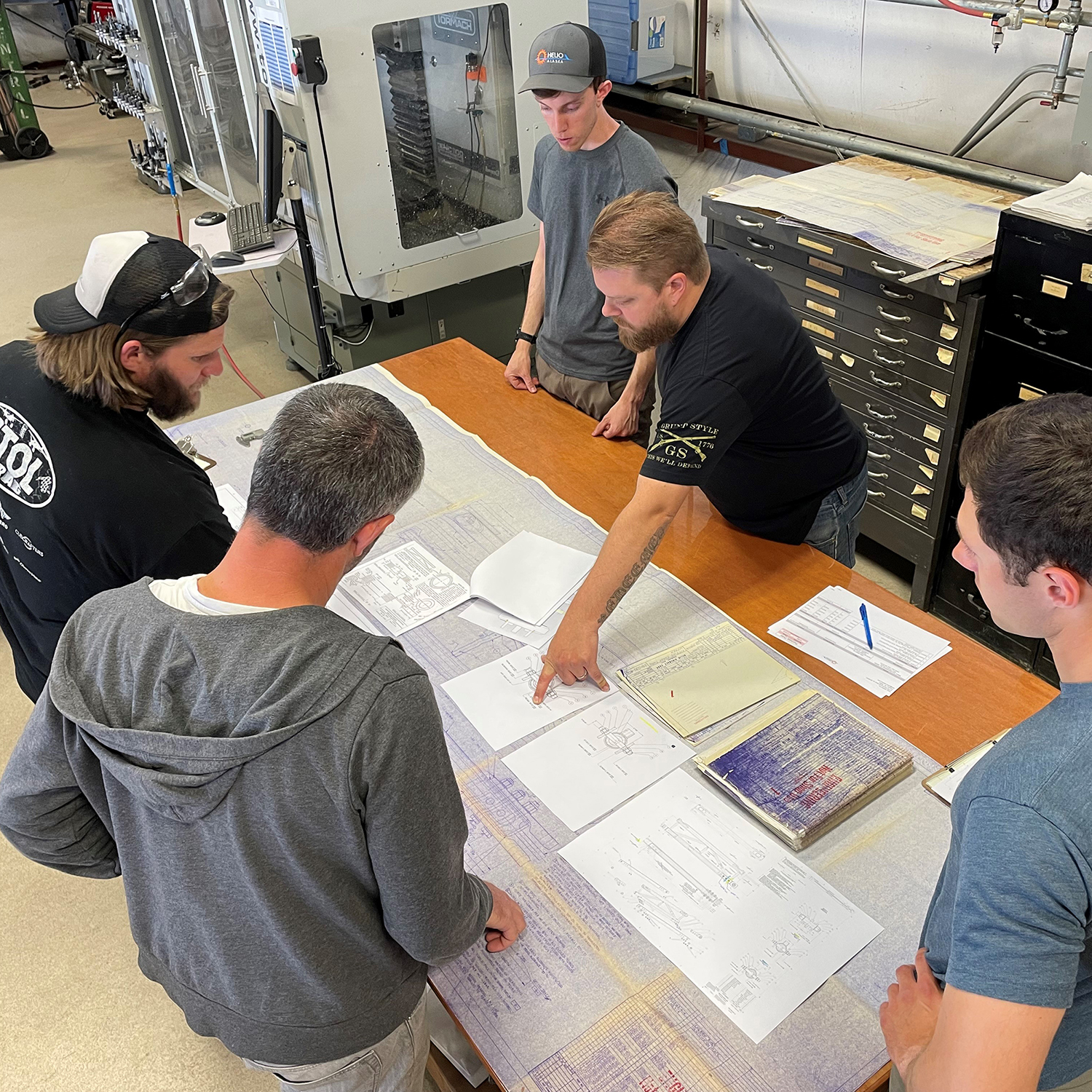 Several men around a table look at engineering diagrams.