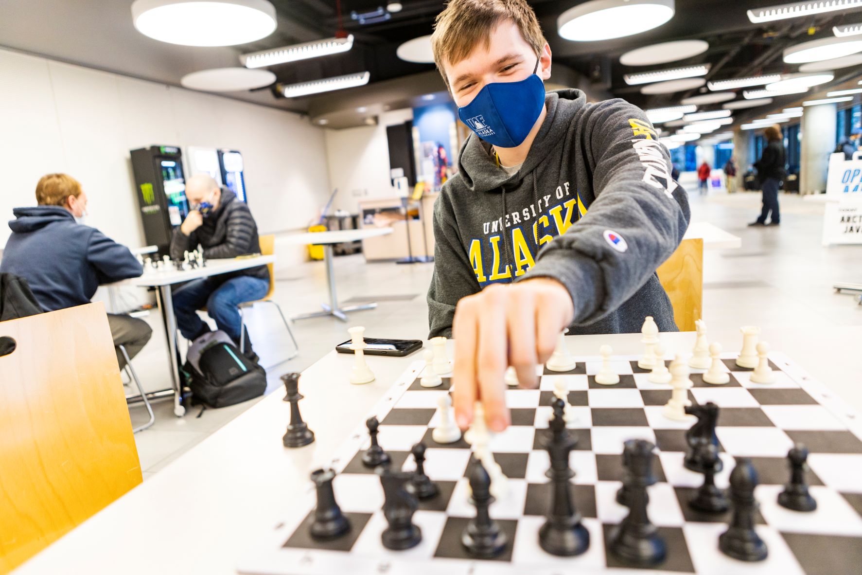 A student wearing a grey UAF hooded sweatshirt plays a game of chess on campus.