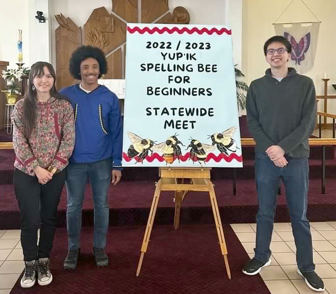 One woman and two men stand alongside a sign that says 