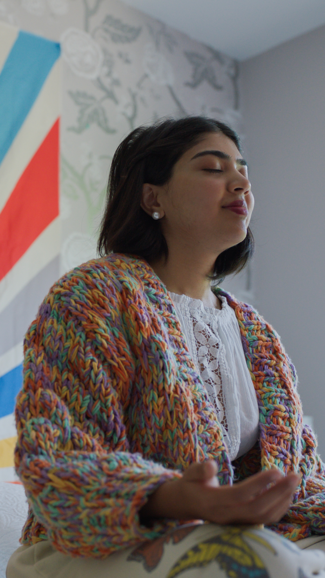 Photo of girl meditating in her room with colorful rainbow tapestry behind her