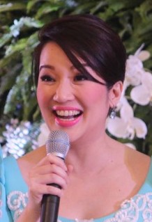 Kris Aquino wearing a light blue dress holding a microphone in her right hand and smiling
