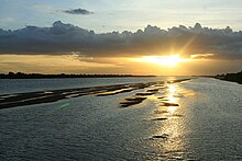 A broad river wi laund pairtially visible at each side; a narrae island separates twa sides o the river