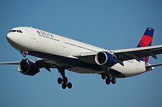 A large twin-engined jet aircraft with its landing gear down. The plane is painted white, with a navy and blue vertical stabilizer, and blue jet engine housings.