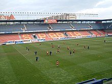 Stade de football avec plusieurs joueurs en bleu, ou en rouge, jouant au football.